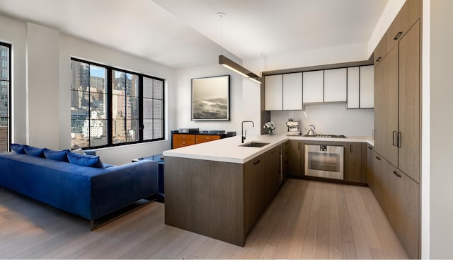 kitchen with light countertops, a peninsula, light wood-style floors, stainless steel appliances, and a sink