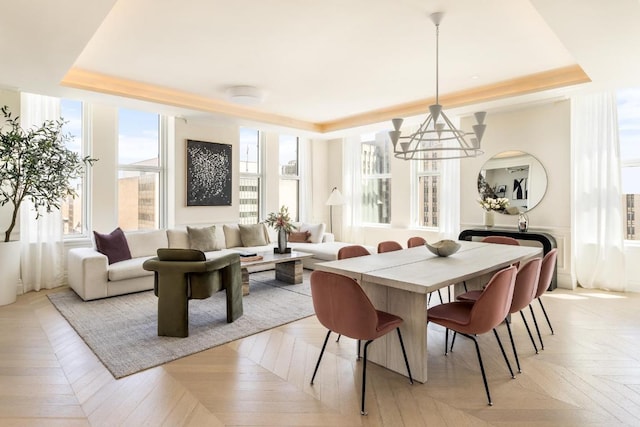 dining space with a chandelier, a raised ceiling, and light parquet floors