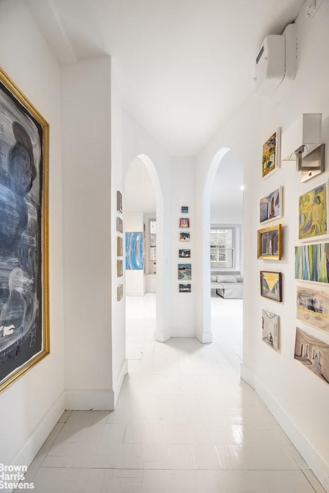 corridor with a wall unit AC, baseboards, and arched walkways