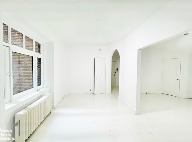 unfurnished room featuring radiator, arched walkways, and baseboards