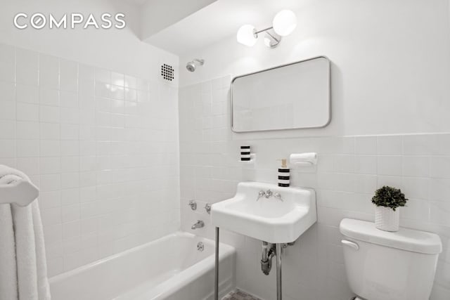 bathroom featuring toilet, tiled shower / bath combo, and tile walls