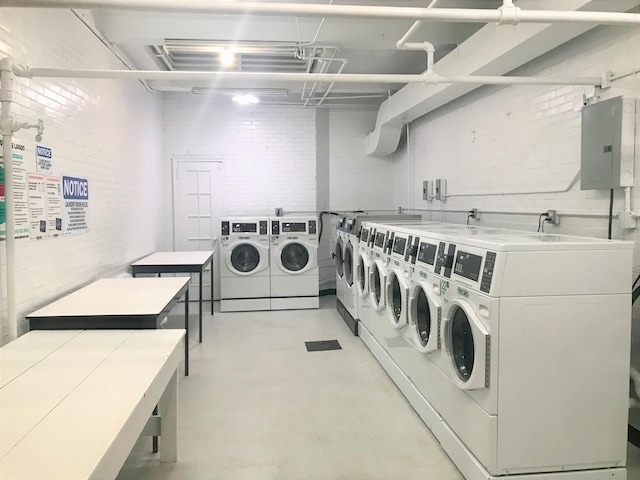 common laundry area with washer and dryer, electric panel, and brick wall