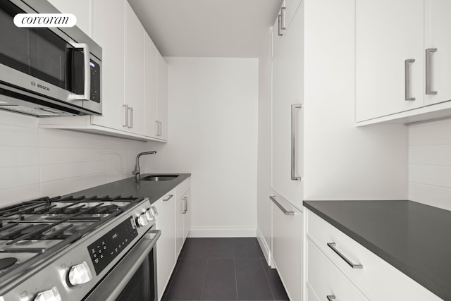 kitchen featuring appliances with stainless steel finishes, dark countertops, white cabinets, and a sink