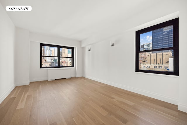 spare room with radiator, light wood-style flooring, visible vents, and baseboards