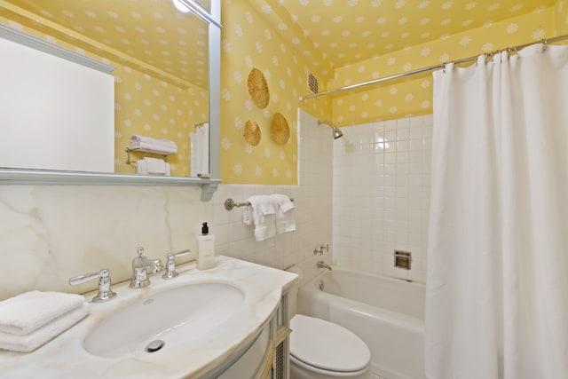 bathroom with toilet, vanity, wainscoting, shower / bath combo with shower curtain, and wallpapered walls