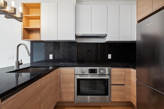 kitchen featuring oven, open shelves, under cabinet range hood, a sink, and freestanding refrigerator