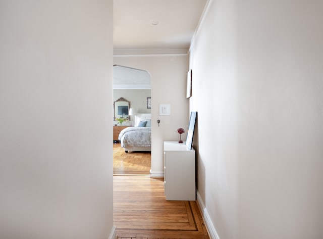 hallway with arched walkways, parquet floors, crown molding, and baseboards