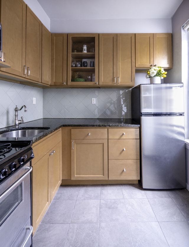 kitchen with dark stone counters, appliances with stainless steel finishes, brown cabinetry, and a sink