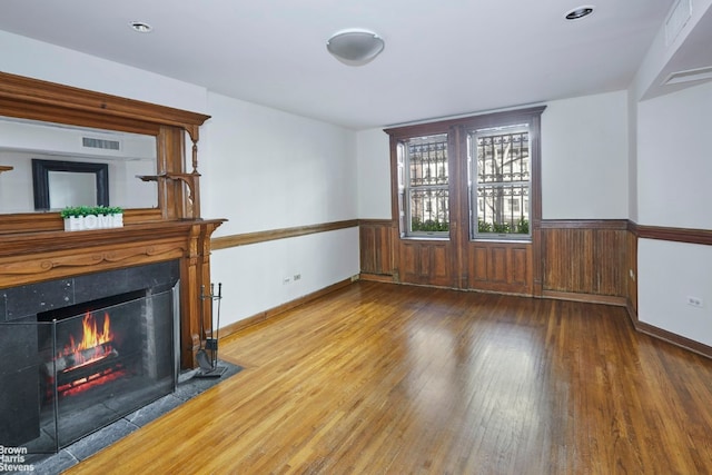 unfurnished living room with a wainscoted wall, a fireplace with flush hearth, visible vents, and wood finished floors