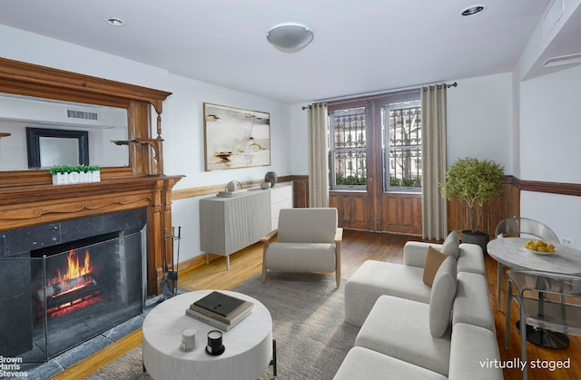 living area with visible vents, a lit fireplace, and wood finished floors