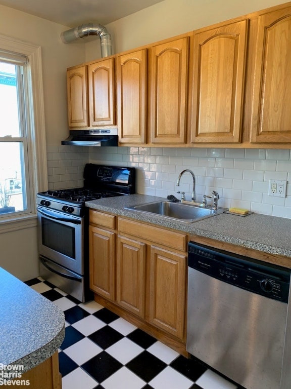 kitchen featuring under cabinet range hood, stainless steel appliances, a sink, a healthy amount of sunlight, and light floors