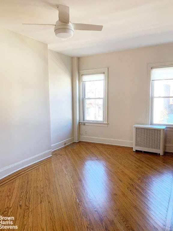 empty room with baseboards, a healthy amount of sunlight, wood finished floors, and radiator