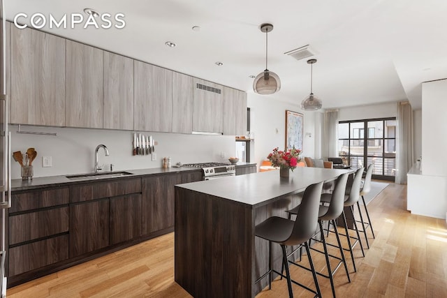 kitchen with stainless steel stove, a sink, hanging light fixtures, dark countertops, and modern cabinets