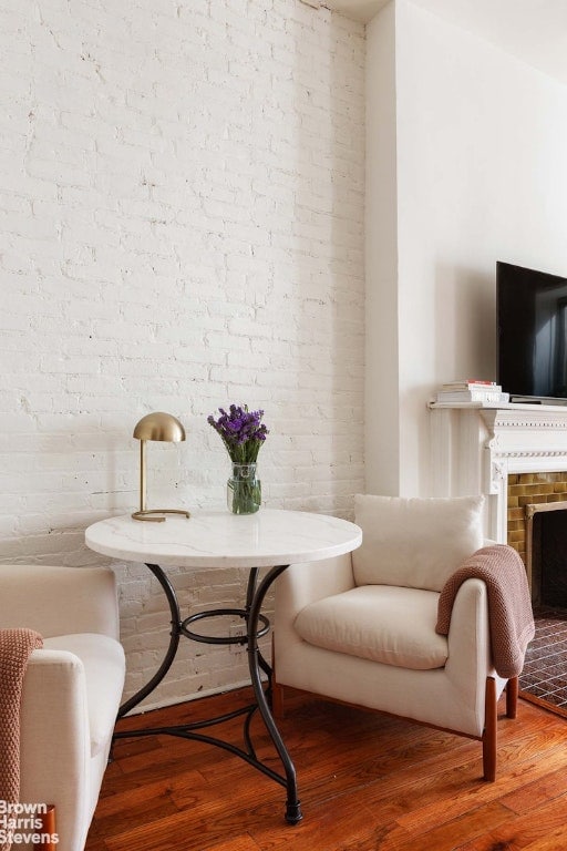 sitting room with brick wall, wood-type flooring, and a brick fireplace