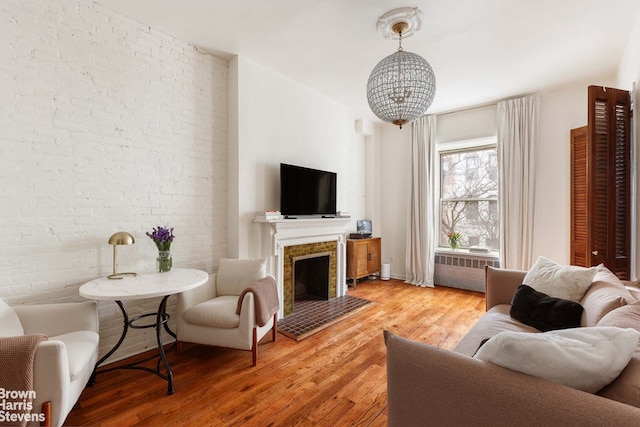 living room featuring radiator heating unit, wood-type flooring, a brick fireplace, and brick wall