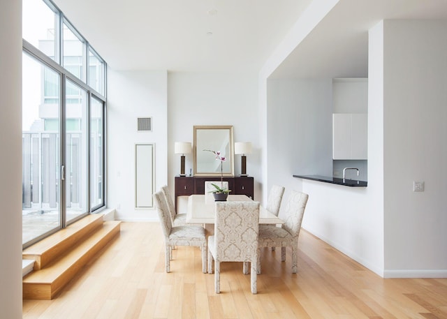 dining space with a wall of windows, light wood-type flooring, visible vents, and baseboards