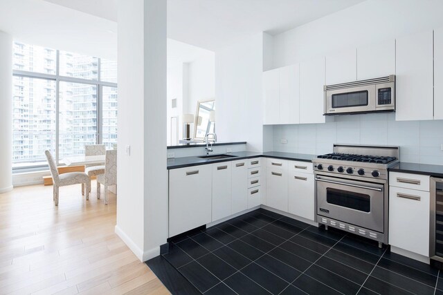 kitchen featuring a sink, white cabinets, appliances with stainless steel finishes, backsplash, and dark countertops