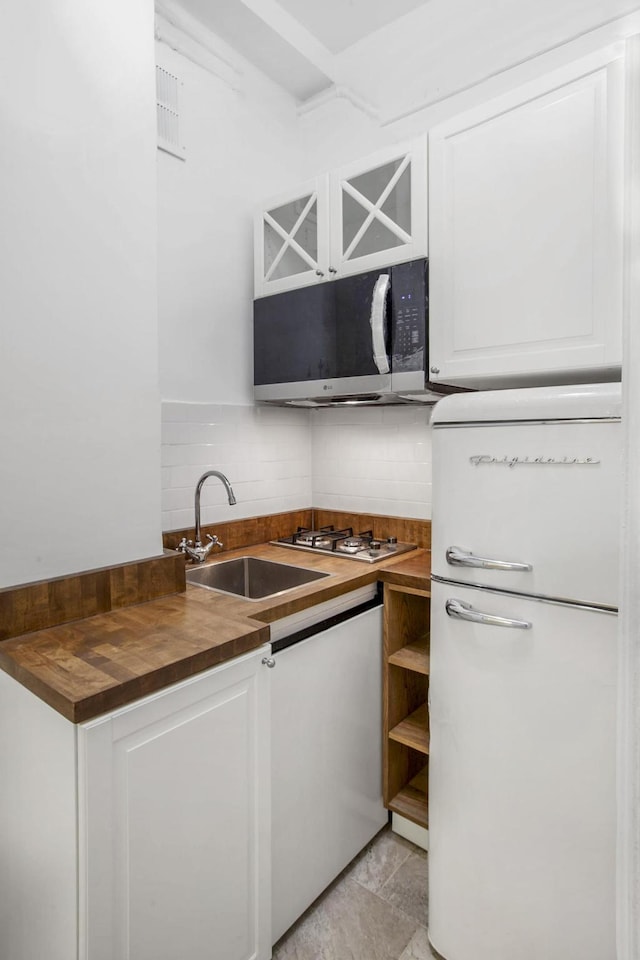 kitchen with white cabinets, butcher block counters, freestanding refrigerator, stainless steel gas stovetop, and a sink