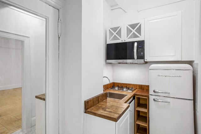 kitchen featuring stainless steel gas cooktop, white cabinetry, decorative backsplash, and freestanding refrigerator