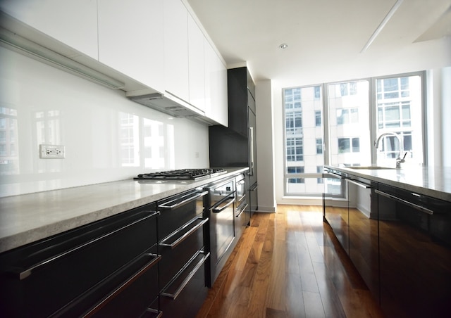 kitchen with stainless steel gas stovetop, sink, white cabinets, dark hardwood / wood-style flooring, and light stone countertops