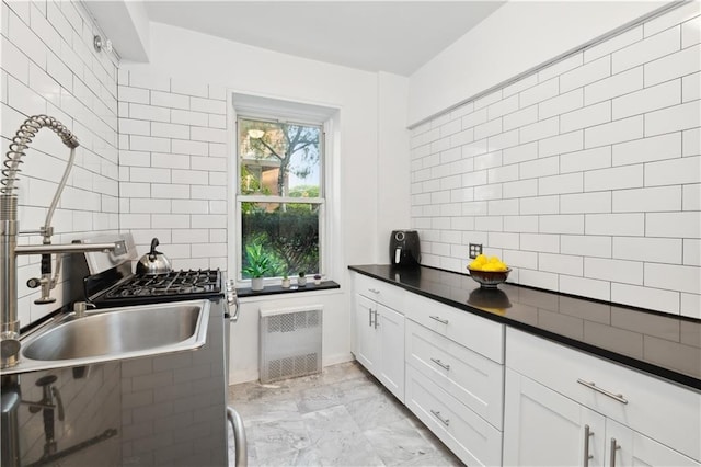 kitchen with dark countertops, backsplash, marble finish floor, white cabinetry, and a sink