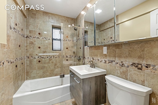 full bathroom featuring vanity, combined bath / shower with glass door, toilet, and tile walls