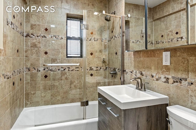 bathroom featuring toilet, enclosed tub / shower combo, tile walls, and vanity