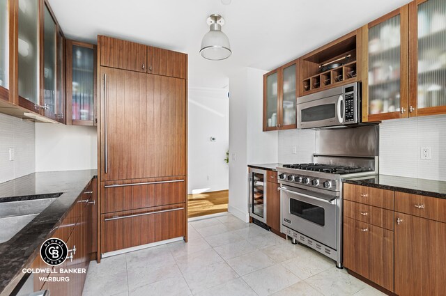 250 E 53rd St Unit 3004, New York City, NY 10022 - kitchen featuring appliances with stainless steel finishes, dark stone counters, backsplash, beverage cooler, and glass insert cabinets