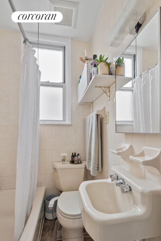 bathroom featuring toilet, a wealth of natural light, shower / bath combination with curtain, and tile walls