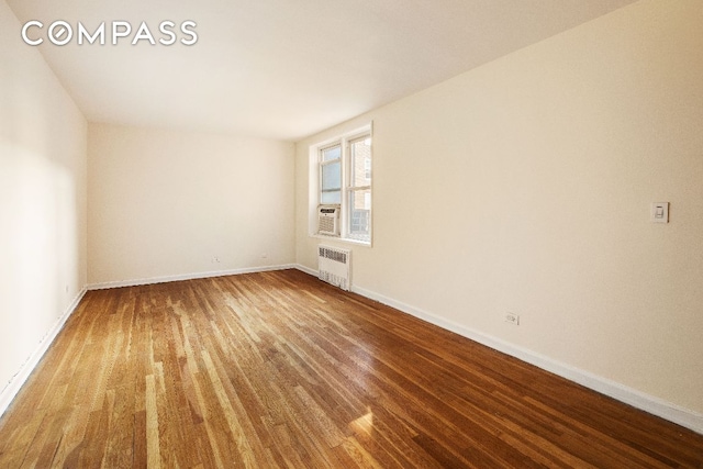 empty room with cooling unit, radiator, baseboards, and wood finished floors