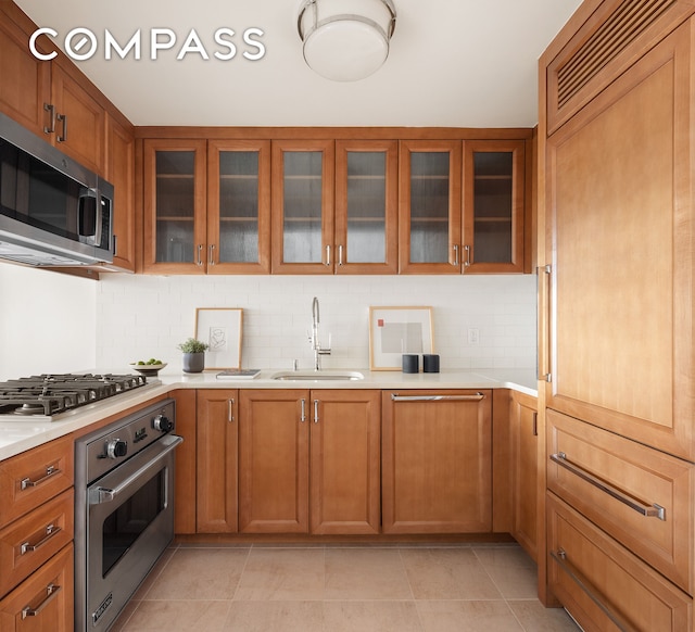 kitchen featuring stainless steel appliances, tasteful backsplash, light countertops, brown cabinetry, and a sink