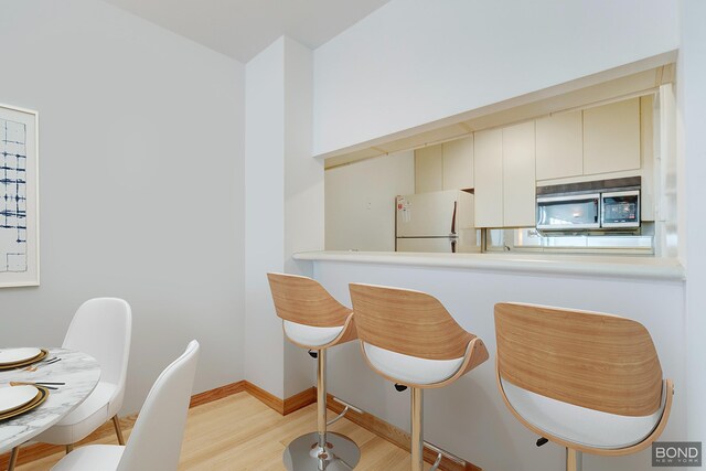 kitchen featuring light wood-style flooring, baseboards, light countertops, freestanding refrigerator, and stainless steel microwave