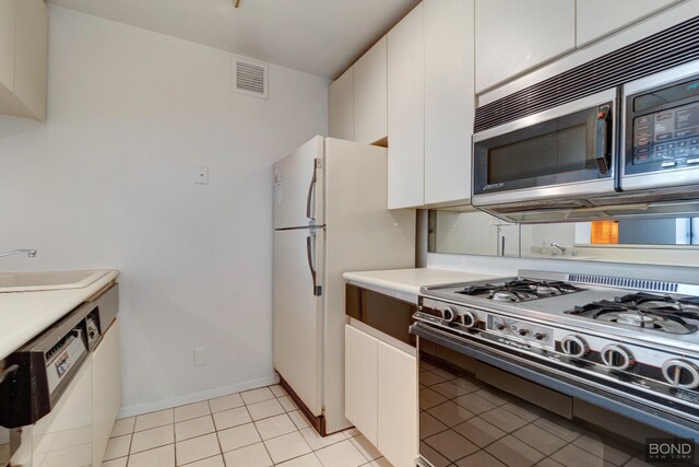 kitchen with a sink, visible vents, white cabinets, stainless steel microwave, and gas range