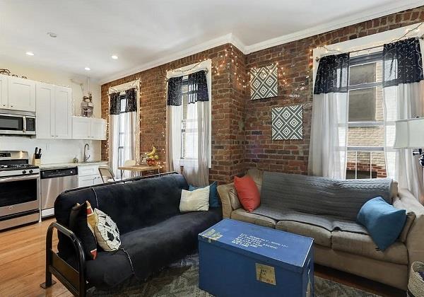 living area with brick wall, ornamental molding, and wood finished floors