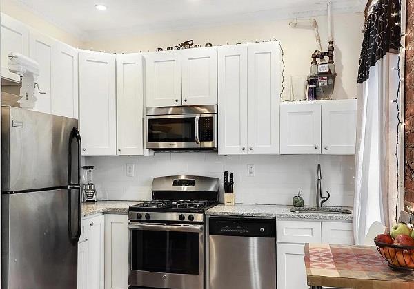 kitchen with white cabinets, light stone counters, stainless steel appliances, and a sink