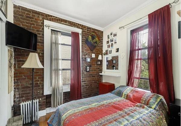 bedroom featuring multiple windows, radiator heating unit, brick wall, and crown molding