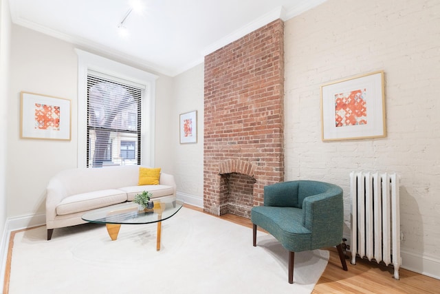 sitting room featuring brick wall, a fireplace, ornamental molding, light wood-type flooring, and radiator