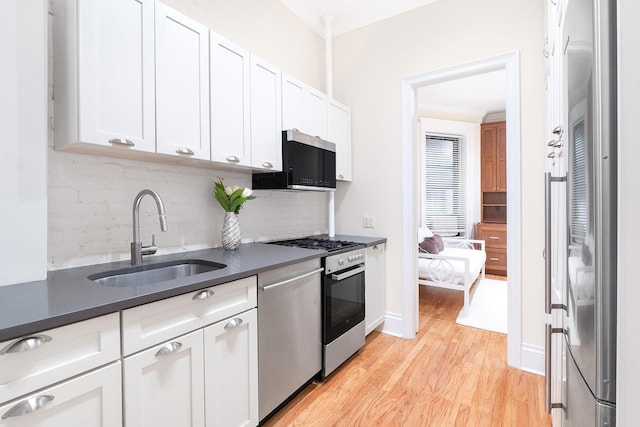 kitchen featuring light wood-style flooring, a sink, dark countertops, white cabinetry, and stainless steel appliances