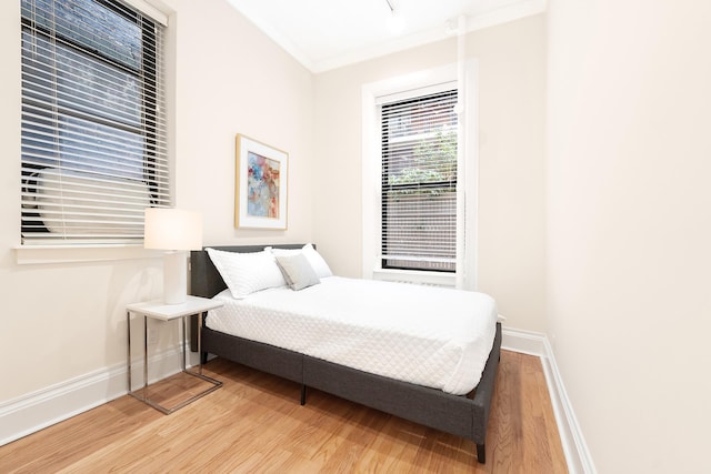 bedroom featuring baseboards, wood finished floors, and crown molding