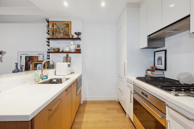 kitchen with light wood-style flooring, stainless steel appliances, light countertops, white cabinetry, and a sink