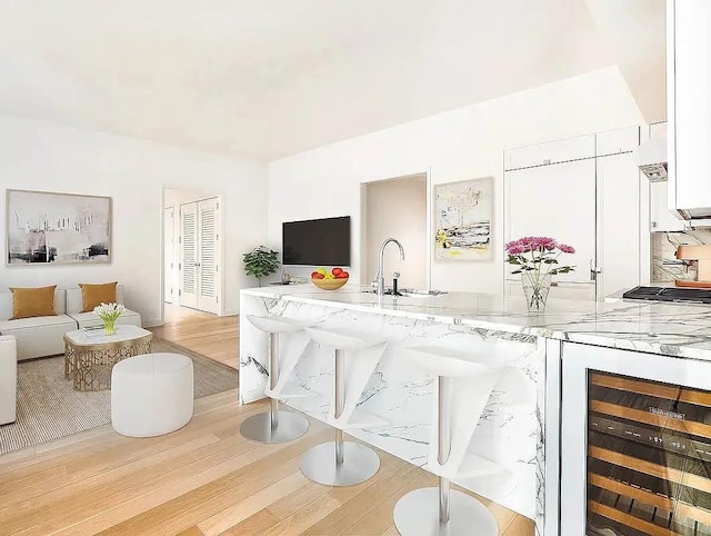 interior space featuring white cabinets, light wood-style flooring, wine cooler, light stone counters, and a sink