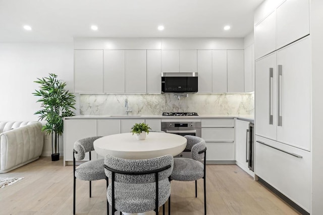 kitchen with white cabinetry, stainless steel appliances, light hardwood / wood-style floors, sink, and tasteful backsplash