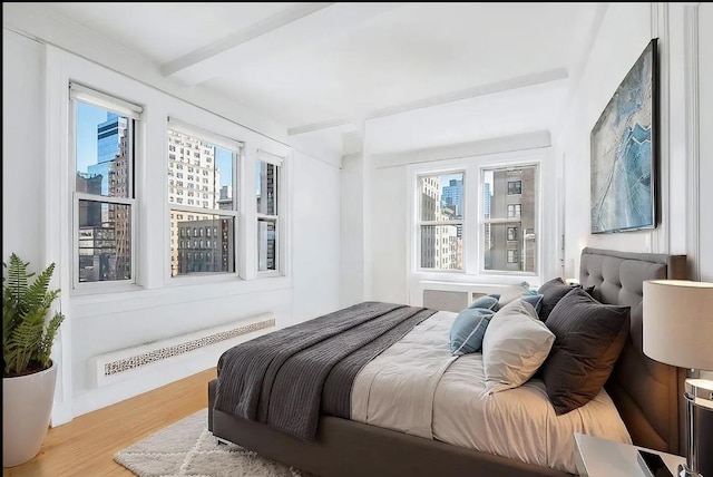 bedroom featuring multiple windows, radiator, beamed ceiling, and light hardwood / wood-style flooring