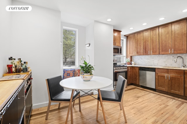 kitchen featuring stainless steel appliances, light wood finished floors, a sink, and decorative backsplash