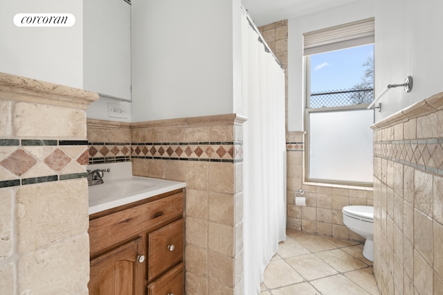 full bath with vanity, wainscoting, toilet, tile walls, and tile patterned floors