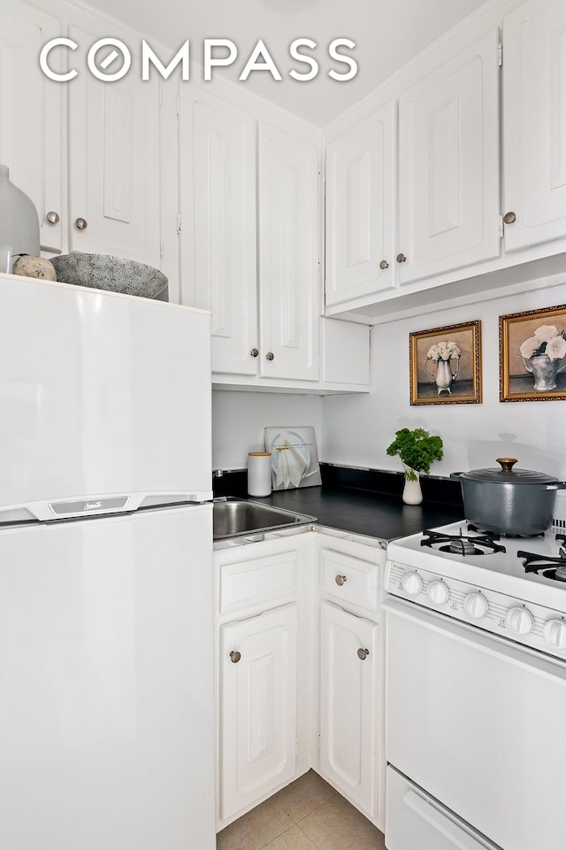 kitchen with white appliances, white cabinets, a sink, and light tile patterned flooring