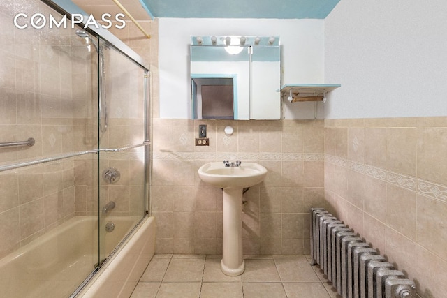 bathroom featuring tile patterned floors, tile walls, shower / bath combination with glass door, and radiator heating unit