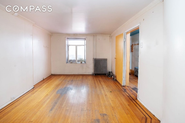 spare room featuring light wood-type flooring, ornamental molding, and radiator heating unit