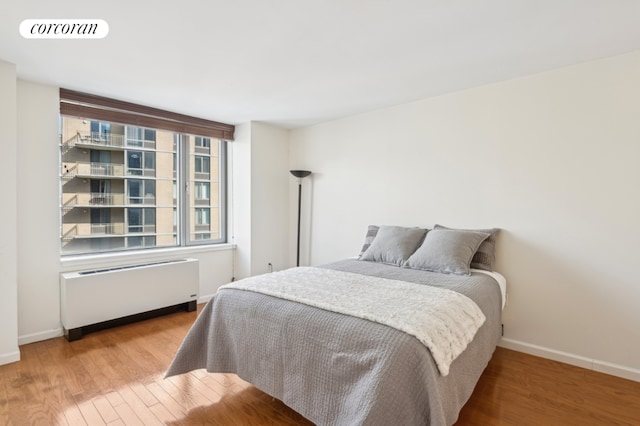 bedroom featuring baseboards, radiator heating unit, visible vents, and wood finished floors