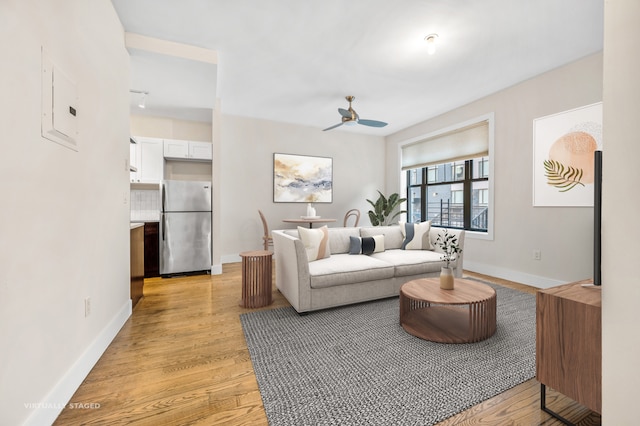 living area featuring ceiling fan, light wood-type flooring, electric panel, and baseboards